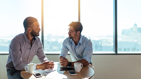 Two businessmen sitting on a coffee table and discussing business matters. Business executives working in their office.